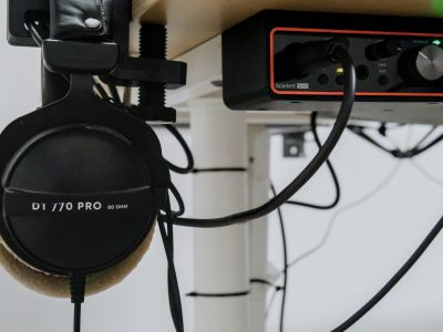 Headphones hanging beside an audio interface and cables under a desk.