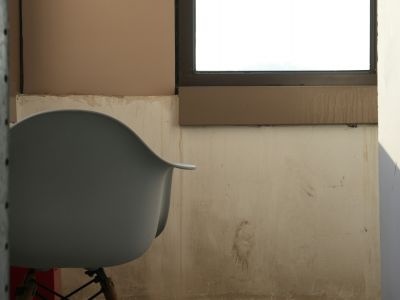 A single empty chair beside a bright window in an otherwise bare room.