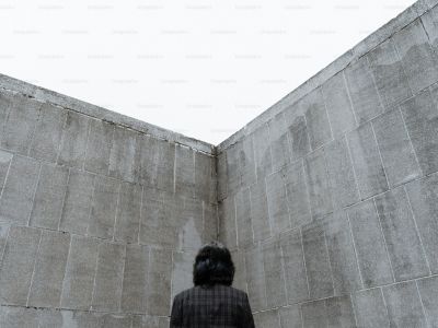 A person standing in the corner of two high concrete walls, seen from behind, looking up.